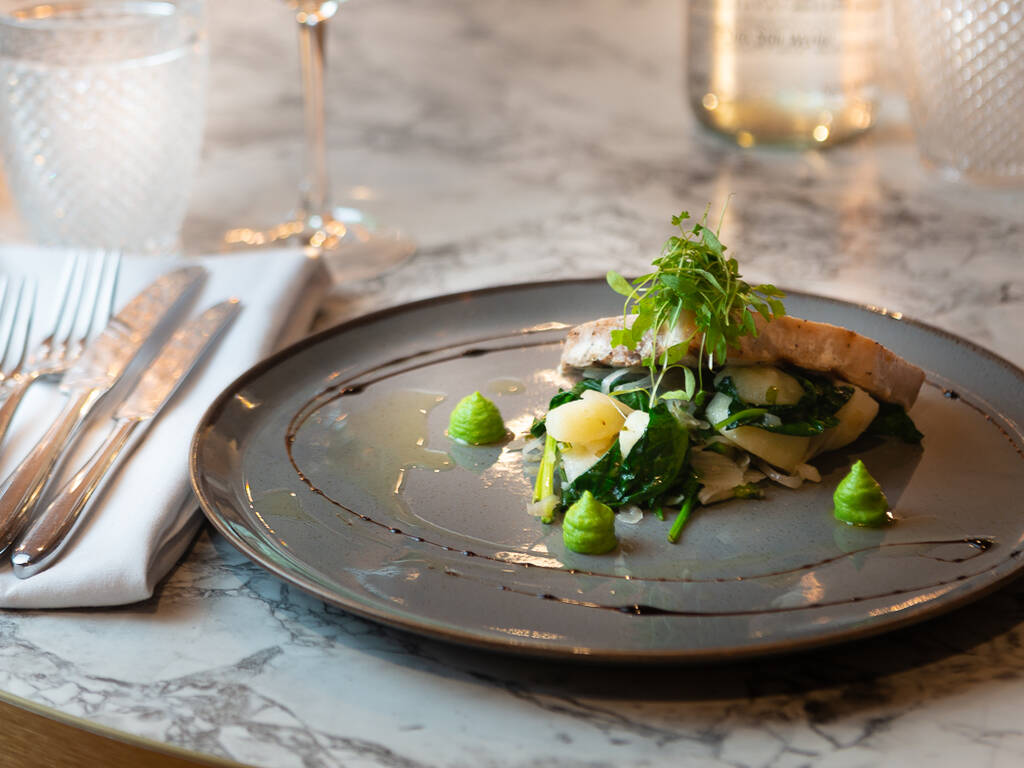 A plate of food, a glass of white wine and a bottle of water on a table at the thyme at the manor restaurant