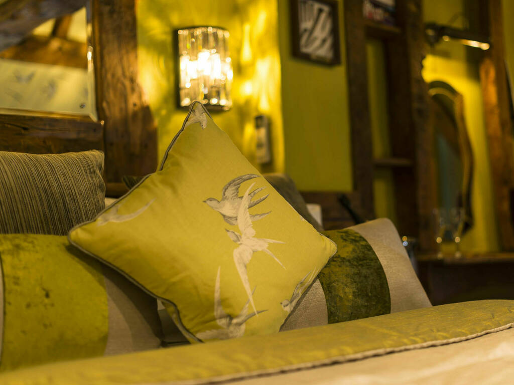 A close up image of the Swallows Suite bed with mood lighting and green pillows