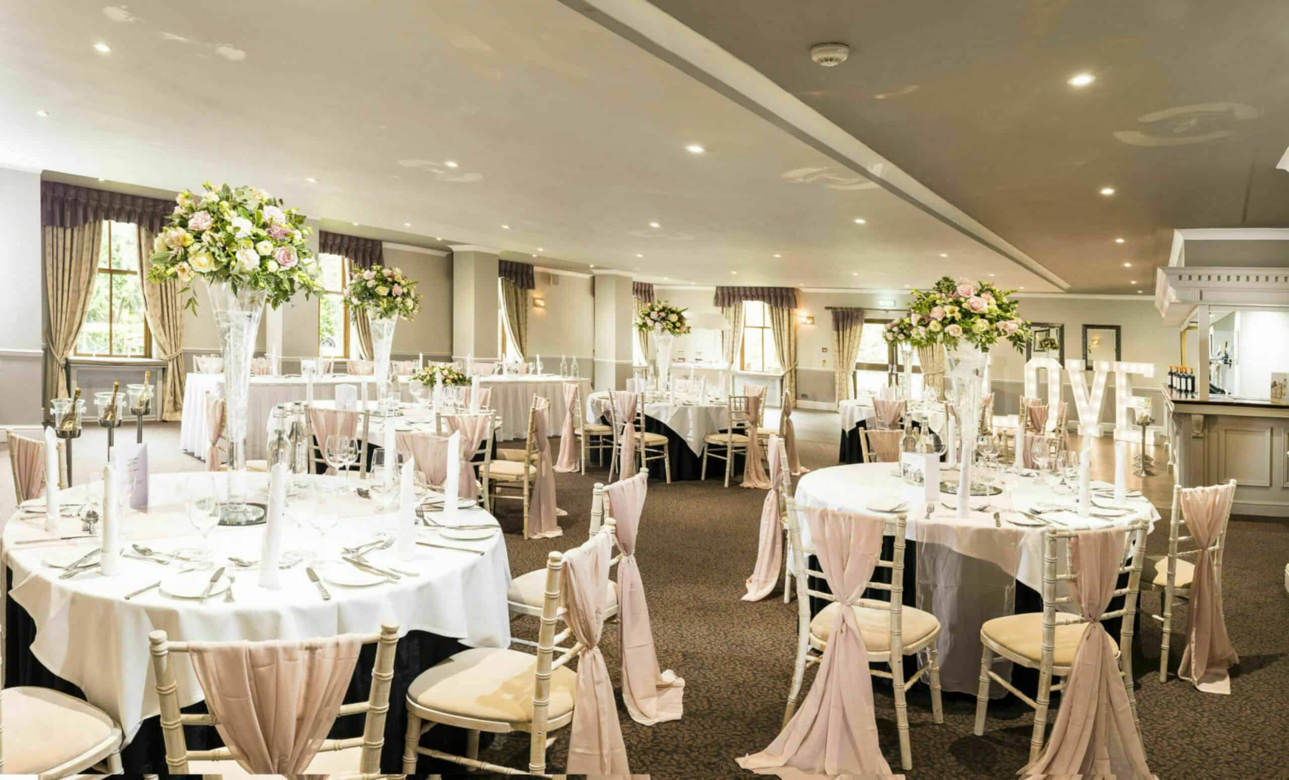 Best wedding venue, Mulberry Suite set up for a wedding, with pink char drapes, flower centrepieces and 'LOVE' light up letters