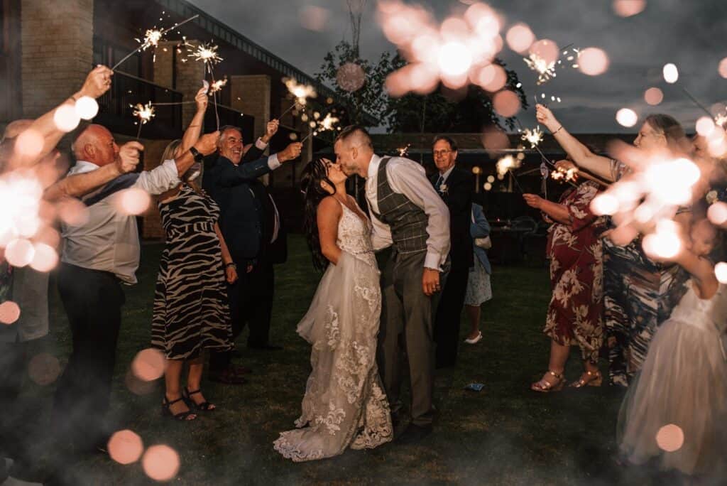 Wedding reviews, Couple kissing outside surrounded by family and friends holding sparklers